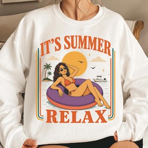 May include: White sweatshirt featuring a graphic of a woman relaxing in a purple inflatable ring in the sea. The design includes the text "IT'S SUMMER RELAX" in orange and a retro style. The image also features a sun, palm trees, and a boat.