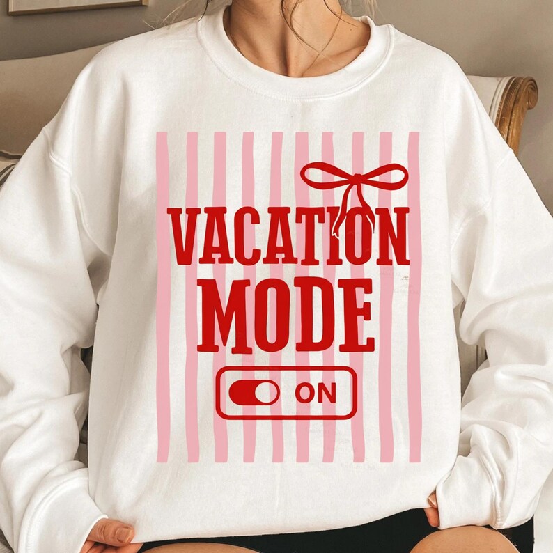May include: White sweatshirt with a red and pink design. The design includes the words "VACATION MODE ON" in a bold, red font, with a red bow and pink vertical stripes. The sweatshirt is a casual, comfortable style.