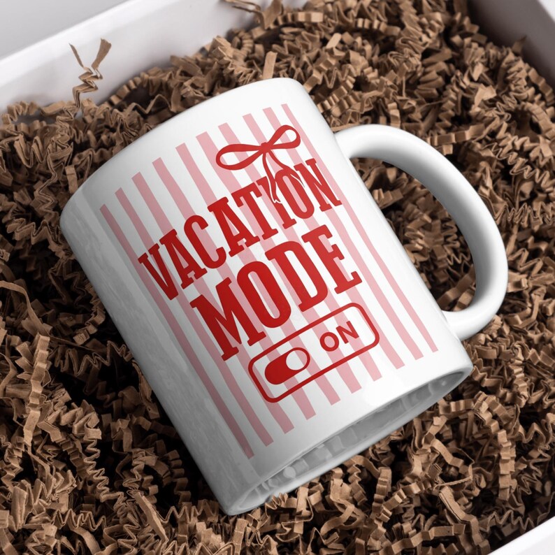May include: White ceramic mug with a red and pink striped pattern and the words "VACATION MODE ON" printed in red. The mug has a white handle and is presented in a white box with brown paper filler.