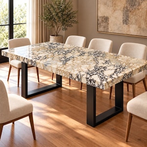 May include: A rectangular dining table featuring a polished stone top with a complex pattern of cream, tan, and black pebble-like shapes. The table is supported by two thick, matte black metal U-shaped legs and is surrounded by six upholstered chairs.