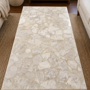 May include: A rectangular coffee table featuring a top surface composed of numerous irregular, light-coloured stone fragments set in a smooth, polished finish. The stone pieces exhibit varying shades of white, cream, and pale grey, creating a mosaic pattern.