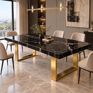 May include: A rectangular dining table featuring a polished black marble top with prominent gold veining, supported by two thick, brushed gold metal U-shaped legs. The table is surrounded by six upholstered chairs with light beige fabric.