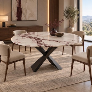 Op de afbeelding: Een ronde eettafel met een wit en donkerrood marmeren blad op een zwart metalen X-vormig onderstel. Vier stoelen met beige gestoffeerde zittingen en donkerhouten frames staan rond de tafel, waarop een donkere vaas en een schaal zijn geplaatst.