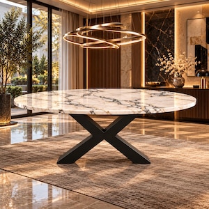 Op de afbeelding: Een ronde eettafel met een wit marmeren blad met opvallende zwarte en grijze aders. De tafel wordt ondersteund door een stevig, matzwart metalen onderstel, ontworpen met een kruisvormig X-frame dat zorgt voor een stabiele basis.