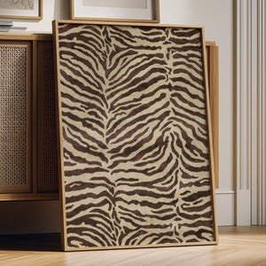 Op de afbeelding: Een rechthoekig ingelijst kunstwerk aan de muur met een contrastrijk zebrastrepenpatroon in donkerbruin en crème. Het kunstwerk is gevat in een dunne, lichtgekleurde houten lijst en toont een herhalend organisch dierenprintontwerp.