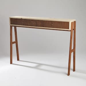 Peut inclure: Une console en bois moderne avec un dessus de couleur claire et deux tiroirs avec un design nervuré. Les pieds sont inclinés et en bois plus foncé. La table mesure environ 122 cm de long.