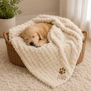 Peut inclure: Un chiot golden retriever dormant dans un panier en osier tressé marron, recouvert d'une couverture en tricot épais couleur crème. La couverture présente une empreinte de patte marron brodée et le nom FORD cousu en lettres marron.