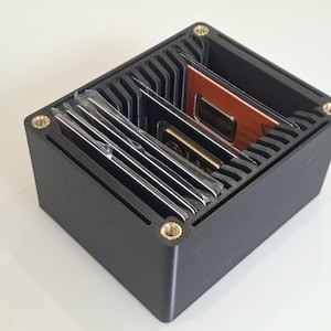 May include: A black rectangular organizer with multiple compartments, holding various small, rectangular items. The organizer has brass-colored screws at each corner. The items inside appear to be electronic components or cards.