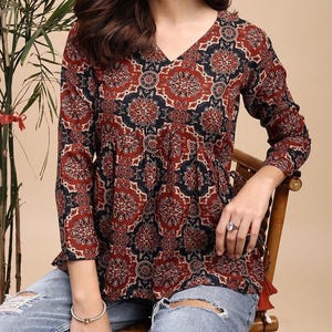 May include: A long-sleeved, V-neck top with a red, navy, and cream floral pattern. The top has a gathered waist and is paired with distressed blue jeans. The sleeves are long and the top is made of a soft material.