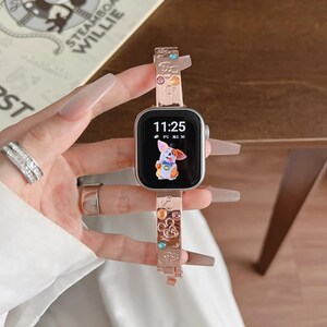 May include: A rose gold smartwatch band featuring embossed Mickey Mouse head silhouettes and embedded multicolored crystals. The watch face displays a digital clock reading 11:25 and a cartoon dog graphic. The band has a metallic finish.
