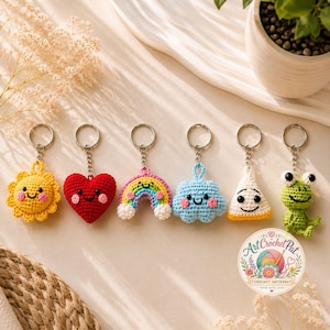 May include: A collection of handmade crochet keychains featuring a smiling sun, heart, rainbow, cloud, triangle, and frog. Each keychain has a silver ring and chain. The keychains are in various colors, including yellow, red, blue, and green.