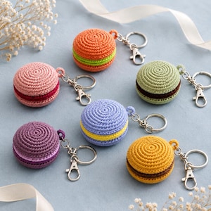 Puede incluir: Seis llaveros de macaron tejidos a ganchillo en varios colores, incluyendo naranja con verde, rosa con rojo oscuro, verde claro con marrón, morado con lila, azul con amarillo y amarillo con marrón, cada uno con una anilla de metal plateado.