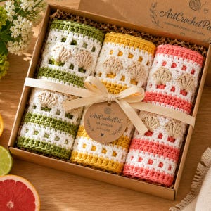 May include: A cardboard gift box containing six handmade crochet washcloths in green, yellow, and coral. Each washcloth has a shell design. The box is tied with a ribbon and a tag that reads "ArtCrochet Pat Handmade with Love."