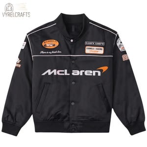 Può includere: Un giubbotto bomber in raso nero con il logo McLaren in bianco e arancione sul petto. La giacca presenta varie toppe a tema automobilistico, tra cui un emblema Formula 1 Racing Team, la scritta There is no finish line e il numero 1963.