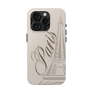 May include: A beige phone case featuring a stylized illustration of the Eiffel Tower and the word "Paris" in a cursive font. The case has a grid pattern background and a camera cutout.