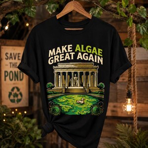 Könnte beinhalten: Ein schwarzes Kurzarm-T-Shirt mit einem Grafikdruck des Lincoln Memorials, einem mit grünen Algen gefüllten Reflexionsbecken und einer kleinen Ente. Der Text "MAKE ALGAE GREAT AGAIN" ist in weißen und grünen Buchstaben über dem Denkmal gedruckt.