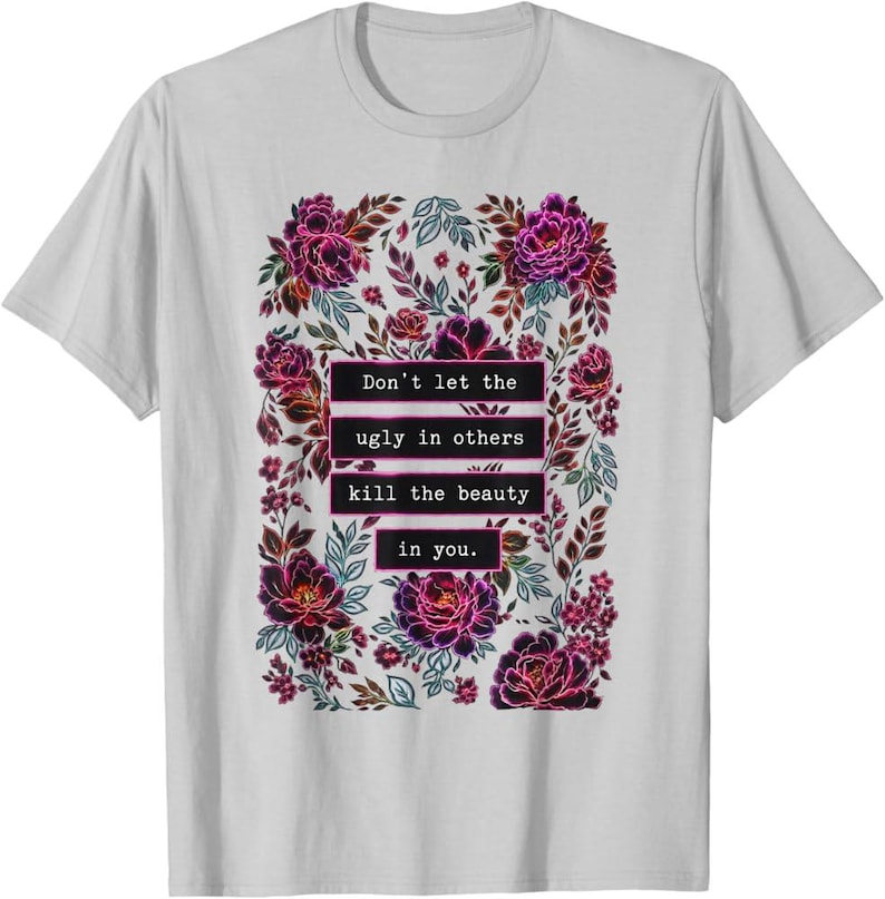 May include: A light gray short-sleeve t-shirt featuring a central rectangular graphic of dark purple and pink flowers and leaves. The text "Don't let the ugly in others kill the beauty in you." is printed in white inside black rectangular bars.