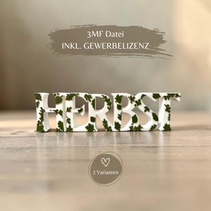 Könnte beinhalten: Ein weißer 3D-gedruckter Schriftzug mit dem Wort HERBST, verziert mit kleinen grünen Blattmotiven. Darüber steht der Text 3MF Datei INKL. GEWERBELIZENZ und darunter befindet sich ein kreisförmiges Abzeichen mit dem Text 2 Varianten und einem Herz.