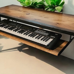 May include: A wooden table with black hairpin legs and a shelf underneath. A black keyboard is sitting on the shelf. The table is made of wood with a natural finish.