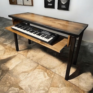 May include: A wooden table with a black metal frame and a pull-out shelf. A black keyboard is on the shelf. The table is in a room with a tiled floor.