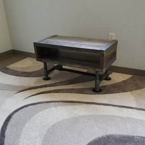 May include: A rustic wooden coffee table with a shelf and black metal pipe legs. The table is on a cream and brown patterned rug.