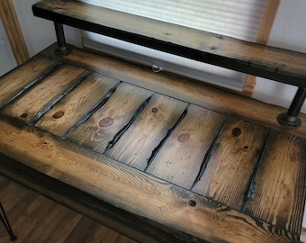 May include: A rustic wooden desk with a black metal frame and a top shelf. The desk has a distressed wood finish and is made of reclaimed wood.