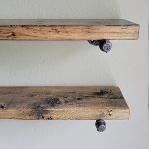 May include: Two rustic wooden shelves with black metal pipe brackets. The shelves are made of reclaimed wood and have a natural finish. The brackets are industrial-style and add a touch of modern design.