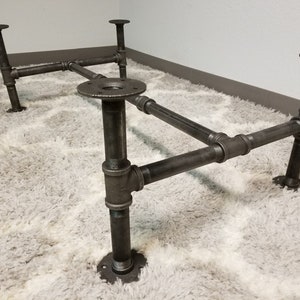 May include: A black metal table base with four legs and a rectangular top. The base is made of industrial pipe fittings.