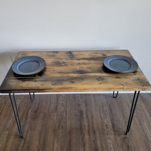 May include: A rustic wooden table with a natural wood finish and black hairpin legs. Two blue ceramic plates are placed on the table.