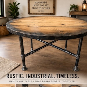 May include: A round dining table with a natural wood grain top featuring a dark, distressed edge and a base constructed from dark gray industrial metal pipes arranged in a cross-brace design. The table surface shows visible knots and wood texture.