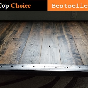 May include: A rustic wooden table top with a metal frame. The wood has a dark brown stain and a distressed finish. The metal frame has a silver finish and is accented with rivets.