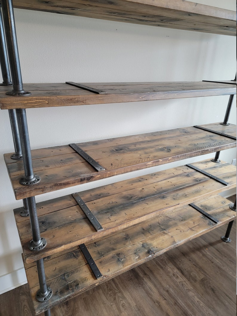 May include: A rustic wooden shelf unit with four shelves supported by black metal pipes. The shelves are made of reclaimed wood with a natural finish and have metal brackets to reinforce the shelves.