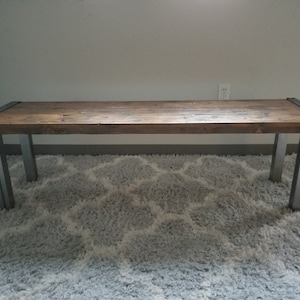 May include: A long wooden bench with a dark brown stain and metal legs. The bench is sitting on a gray shag rug.