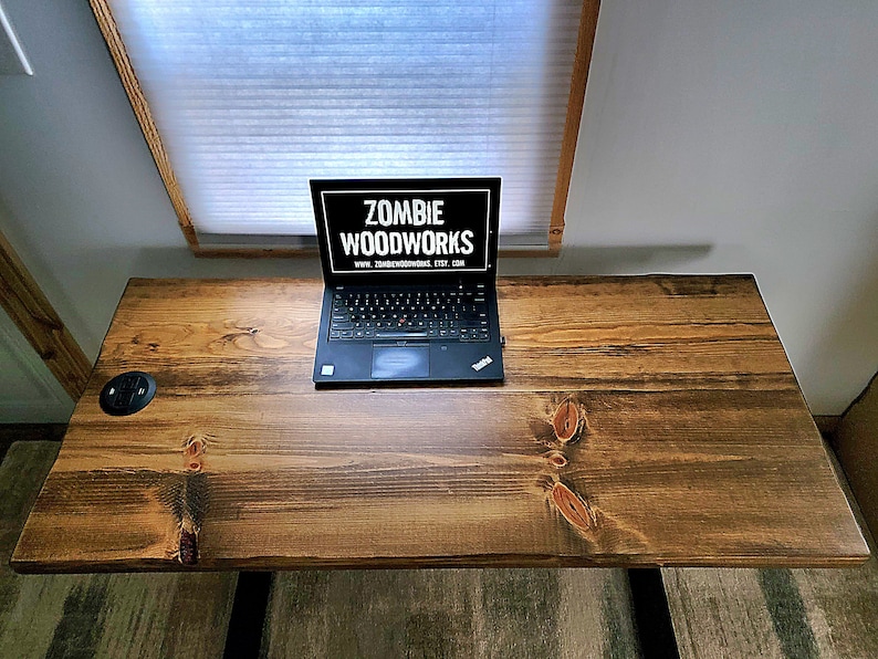 May include: A dark wood desk with a laptop computer on top. The laptop screen displays the text "Zombie Woodworks" and a website address. There is a black electrical outlet on the desk.