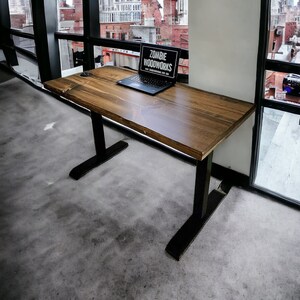 May include: A wooden desk with black metal legs. The desk has a laptop on it with a sticker that says "Zombie Woodworks". The desk is in front of a window with a view of a city skyline.