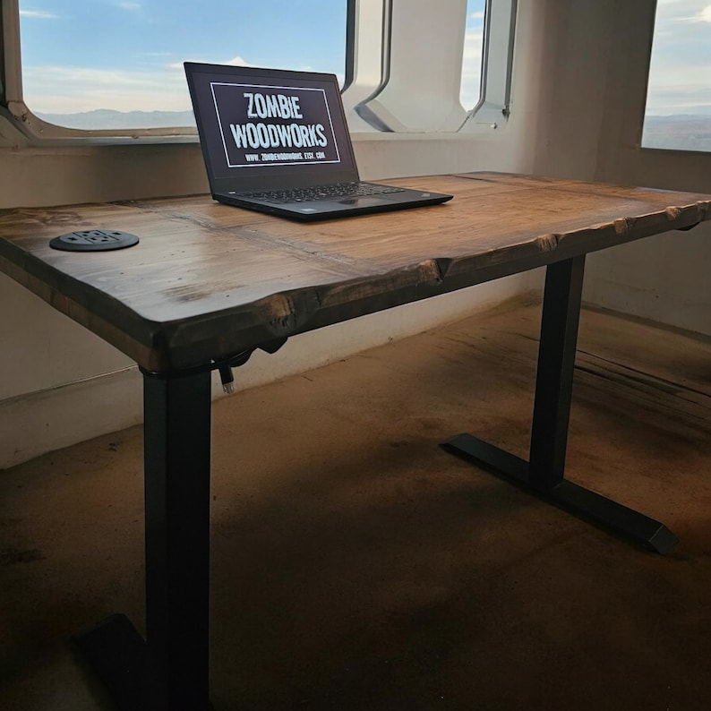 May include: A black standing desk with a wooden top. The desk has a laptop on it and a power strip. The desk is in front of a window with a view of the mountains.