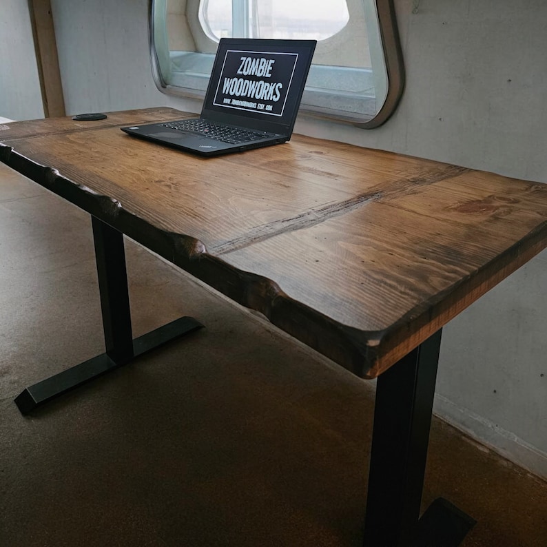 May include: A wooden desk with a live edge top and black metal legs. A laptop computer is on the desk with the text "Zombie Woodworks" on the screen.