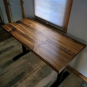 May include: A dark brown wooden desk with black metal legs. The desk has a smooth, polished finish and is sitting on a striped rug.
