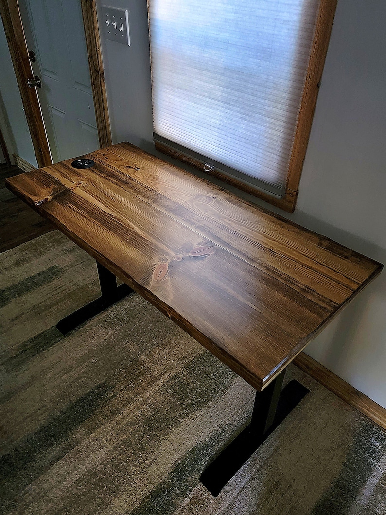May include: A dark brown wooden desk with black metal legs. The desk has a smooth, polished finish and is sitting on a striped rug.