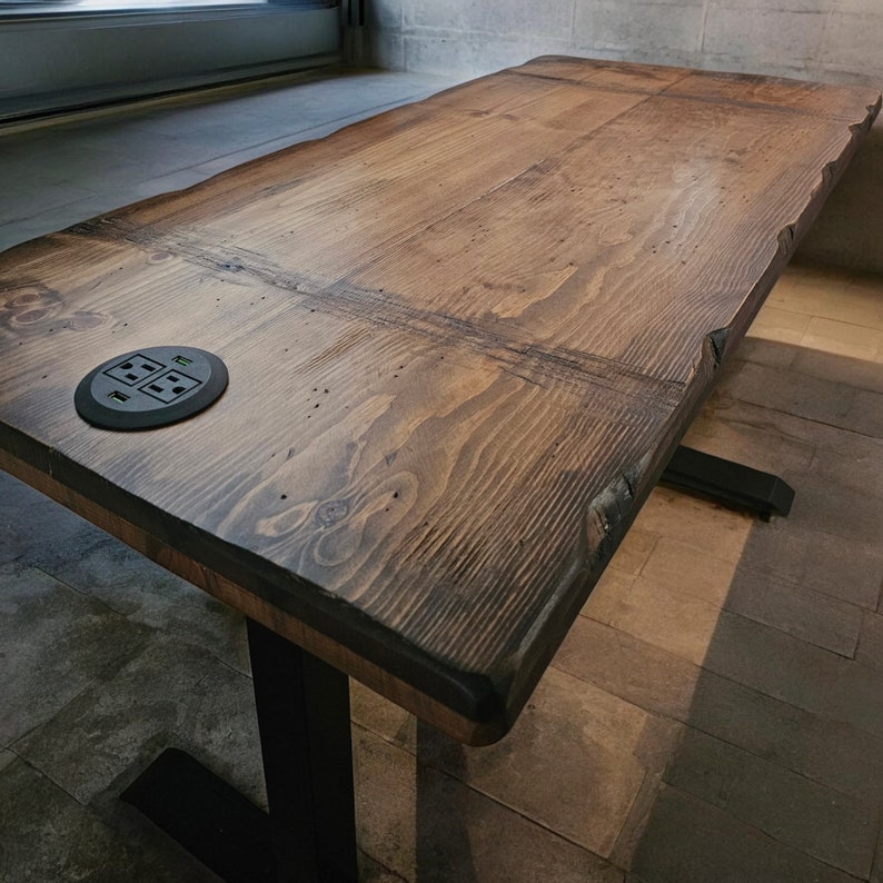 May include: A dark brown wooden desk with a black metal base and a built-in power outlet. The desk has a rustic, reclaimed wood look and is perfect for a home office or workspace.