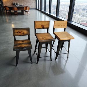 May include: Three rustic wooden chairs with black metal legs. The chairs have a natural wood finish, with visible grain and knots. The chairs are arranged in a row, showcasing their design and construction. The chairs are suitable for a kitchen or dining room.