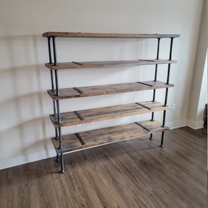 May include: A five-shelf industrial style bookshelf made of reclaimed wood and black metal pipe. The shelves are made of rustic wood with a natural finish. The metal pipes are black and have a matte finish.