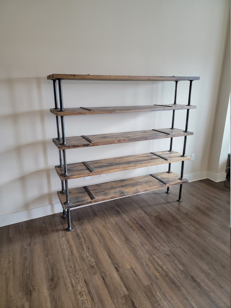 May include: A five-shelf industrial style bookshelf made of reclaimed wood and black metal pipe. The shelves are made of rustic wood with a natural finish. The metal pipes are black and have a matte finish.