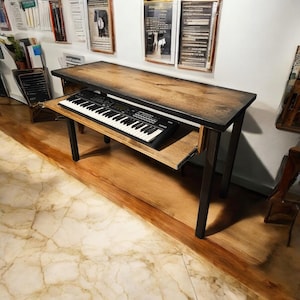 May include: A wooden table with a black metal frame and a pull-out shelf. A black keyboard is on the shelf. The table is in a room with a wooden floor and white walls.