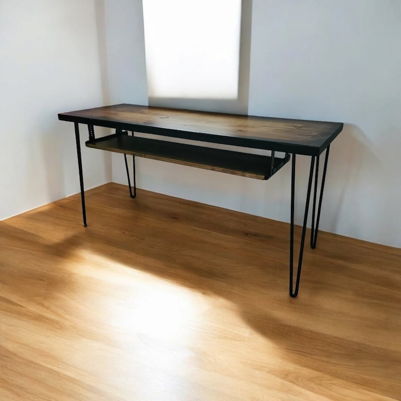 May include: A wooden desk with a black stained top and a lower shelf. The desk has hairpin legs made of black metal.
