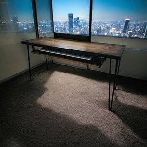 May include: A black metal desk with a wooden top and a pull-out keyboard tray. The desk is in a room with a large window overlooking a city skyline.