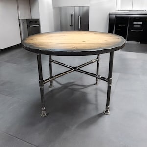 May include: A round wooden table with a black stained edge and a black metal pipe base. The table is in a kitchen setting with a tiled floor.