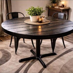 May include: A round, dark wood dining table with a black metal base and legs. The table is set with a plant, candles, and a woven placemat. Two black metal chairs are positioned around the table. The table is set on a patterned rug.