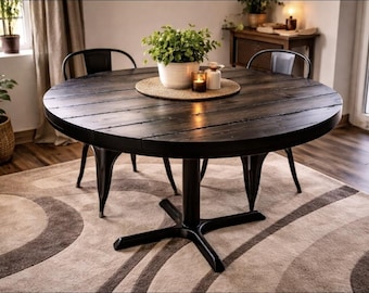 May include: A round, dark wood dining table with a black metal base and legs. The table is set with a plant, candles, and a woven placemat. Two black metal chairs are positioned around the table. The table is set on a patterned rug.