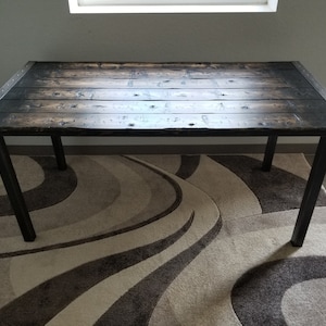 May include: A rustic wooden table with a black stained finish and metal legs. The table is sitting on a patterned rug.